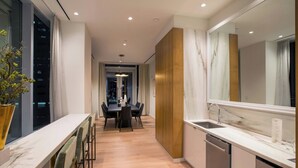A modern kitchen with a marble countertop, a sink, and a dishwasher. There is a dining area with a table and chairs, and a large window on the left side.