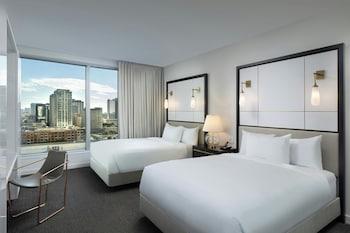 Enjoy a city view from the large window, featuring two single beds with white linens and a modern design. at The Laura Hotel, Houston Downtown, Autograph Collection