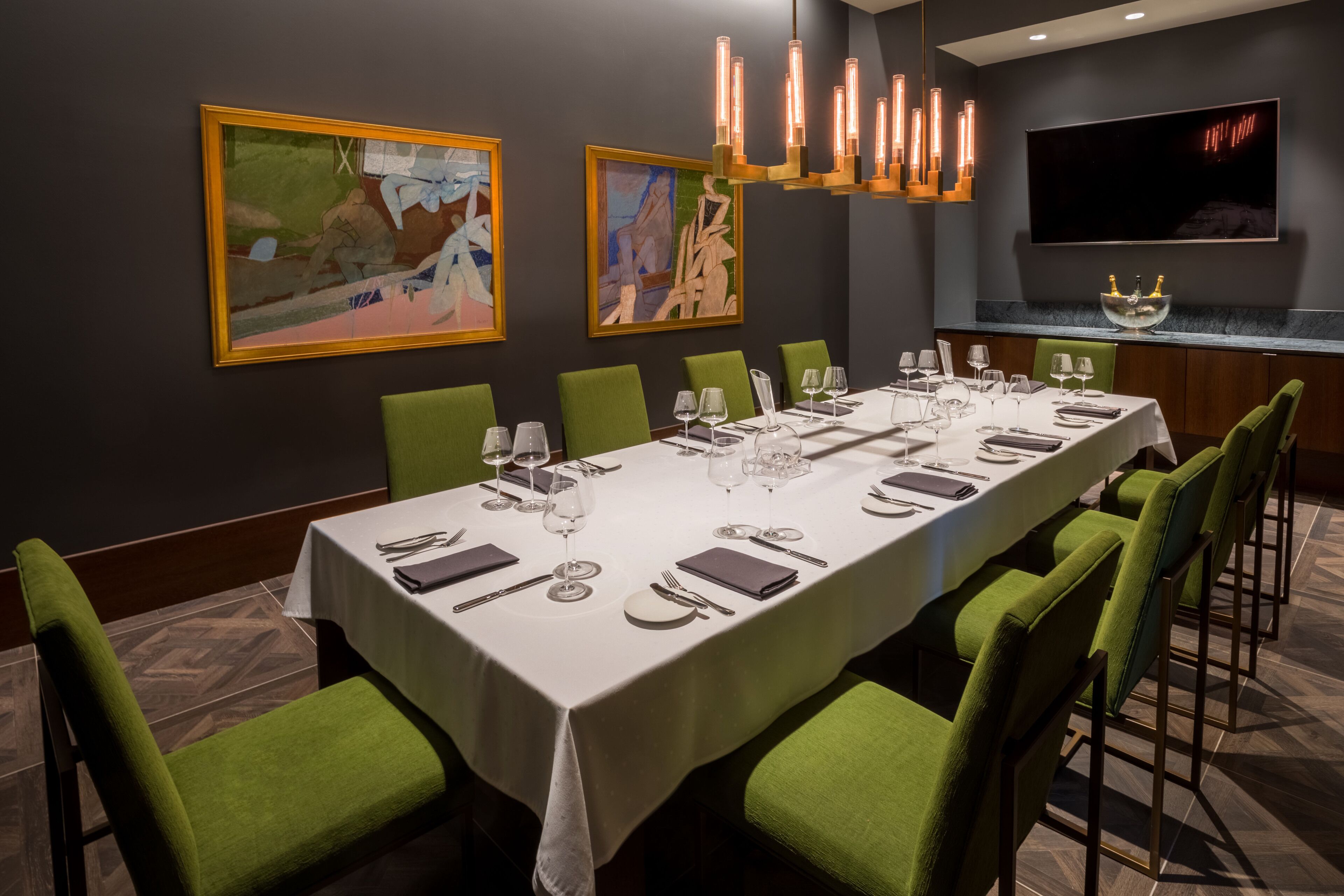 A dining room with a long table set for a meal, green upholstered chairs, and a modern chandelier.