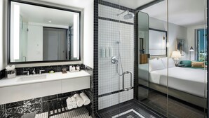 A modern hotel bathroom with a large mirror, a shower, and a bed.