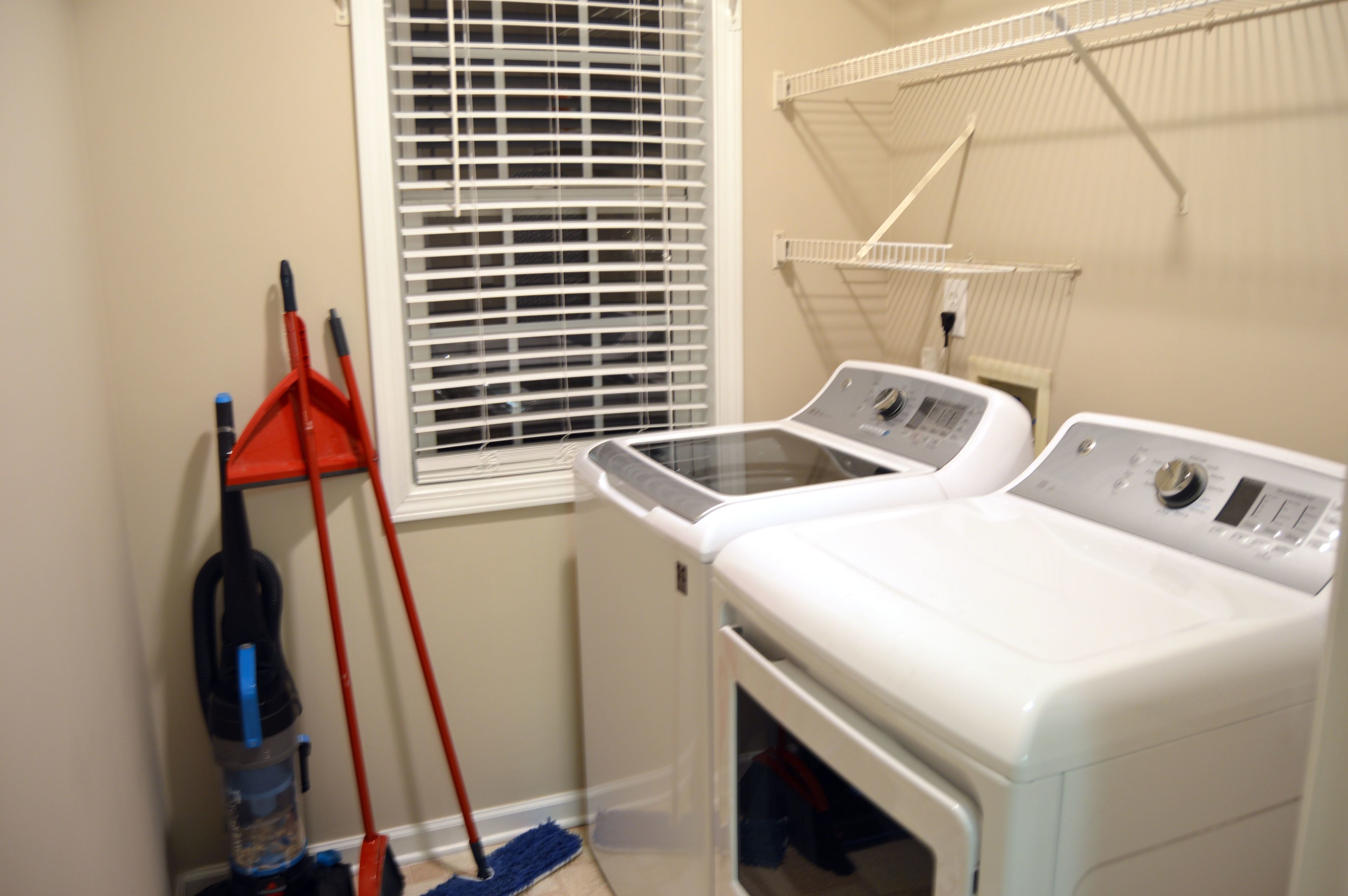 A laundry room with a washing machine, a dryer, a mop, and a broom.