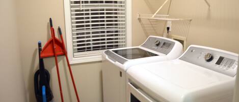 A laundry room with a washing machine, a dryer, a mop, and a broom.