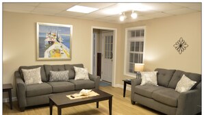 A living room with two grey sofas, a dark coffee table, and a painting of a boat on the wall. - Opis Realty-Spacious Metro Atlanta Home (Conyers)