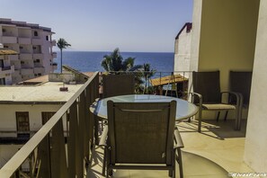 A balcony with a glass table and chairs, overlooking a beach and palm trees. - V177 Condo at Vallarta Romantic Zone (Puerto Vallarta)