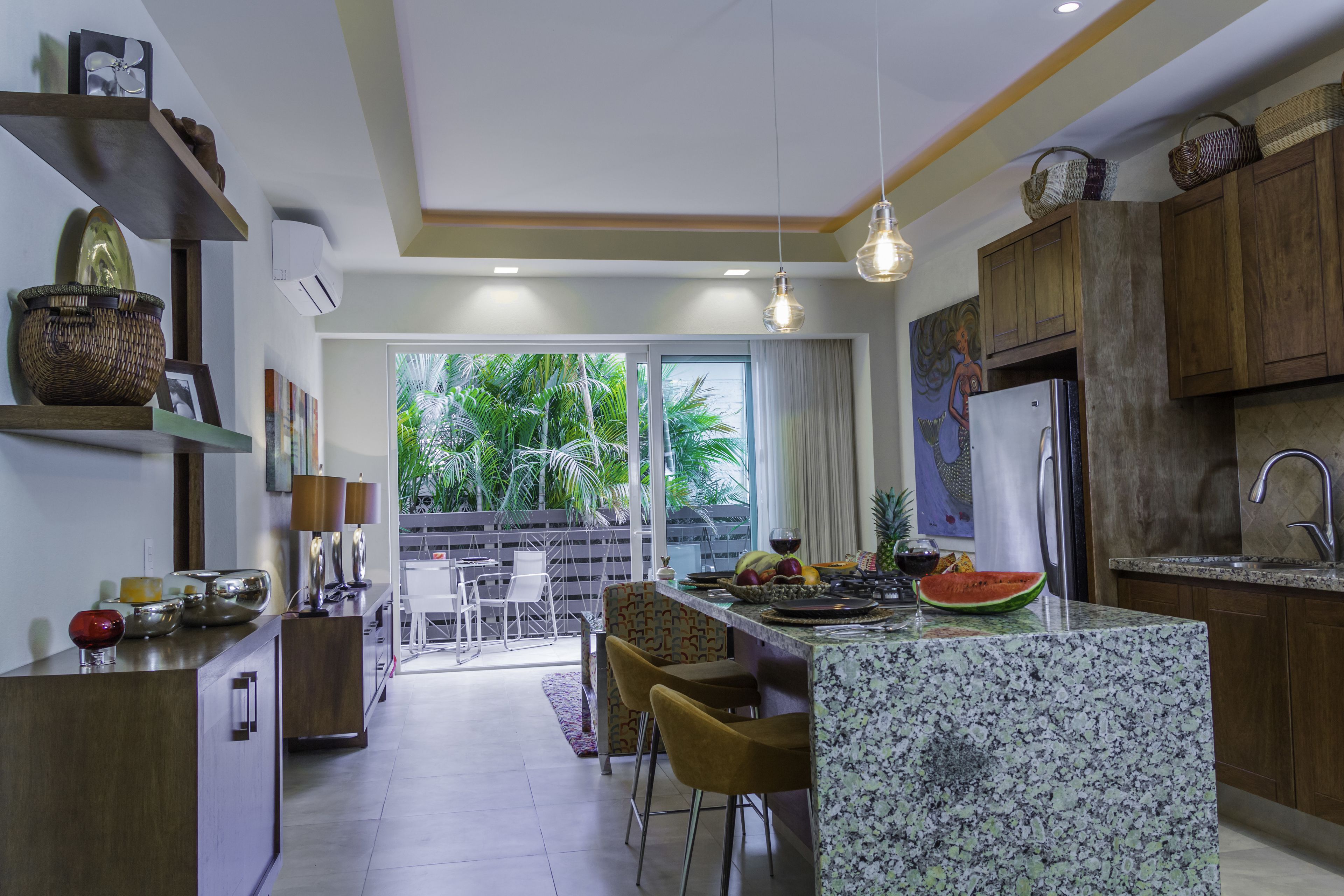Una cocina moderna con una isla central, armarios de madera y vistas a un jardín tropical.