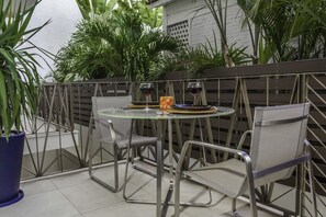 A glass table with metal chairs, two glasses of red wine, and a small plate with a slice of cake on a balcony with potted plants and a wooden fence. - V177 Condo at Vallarta Romantic Zone (Puerto Vallarta)