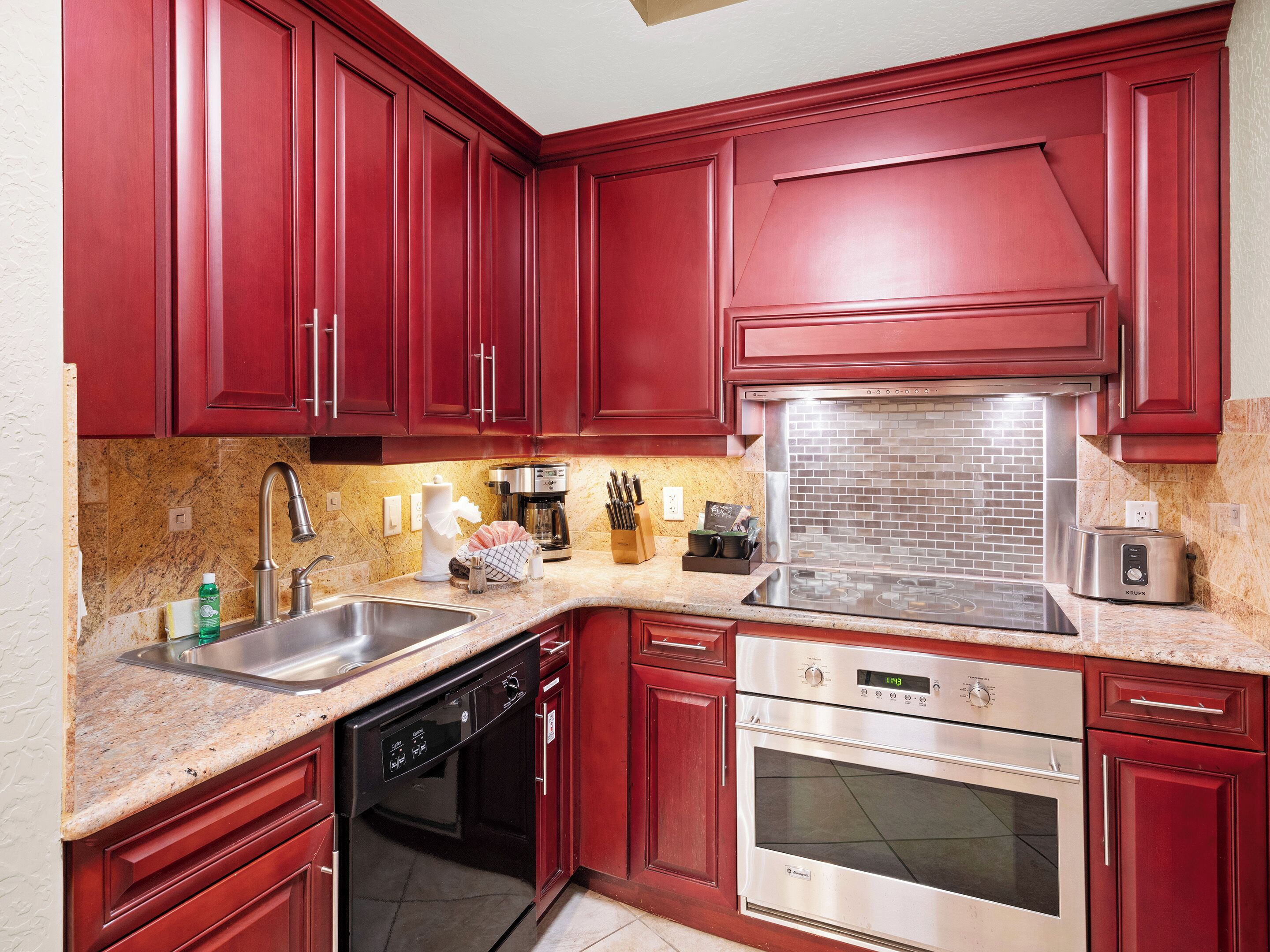 A kitchen with red cabinets, stainless steel appliances, and granite countertops.