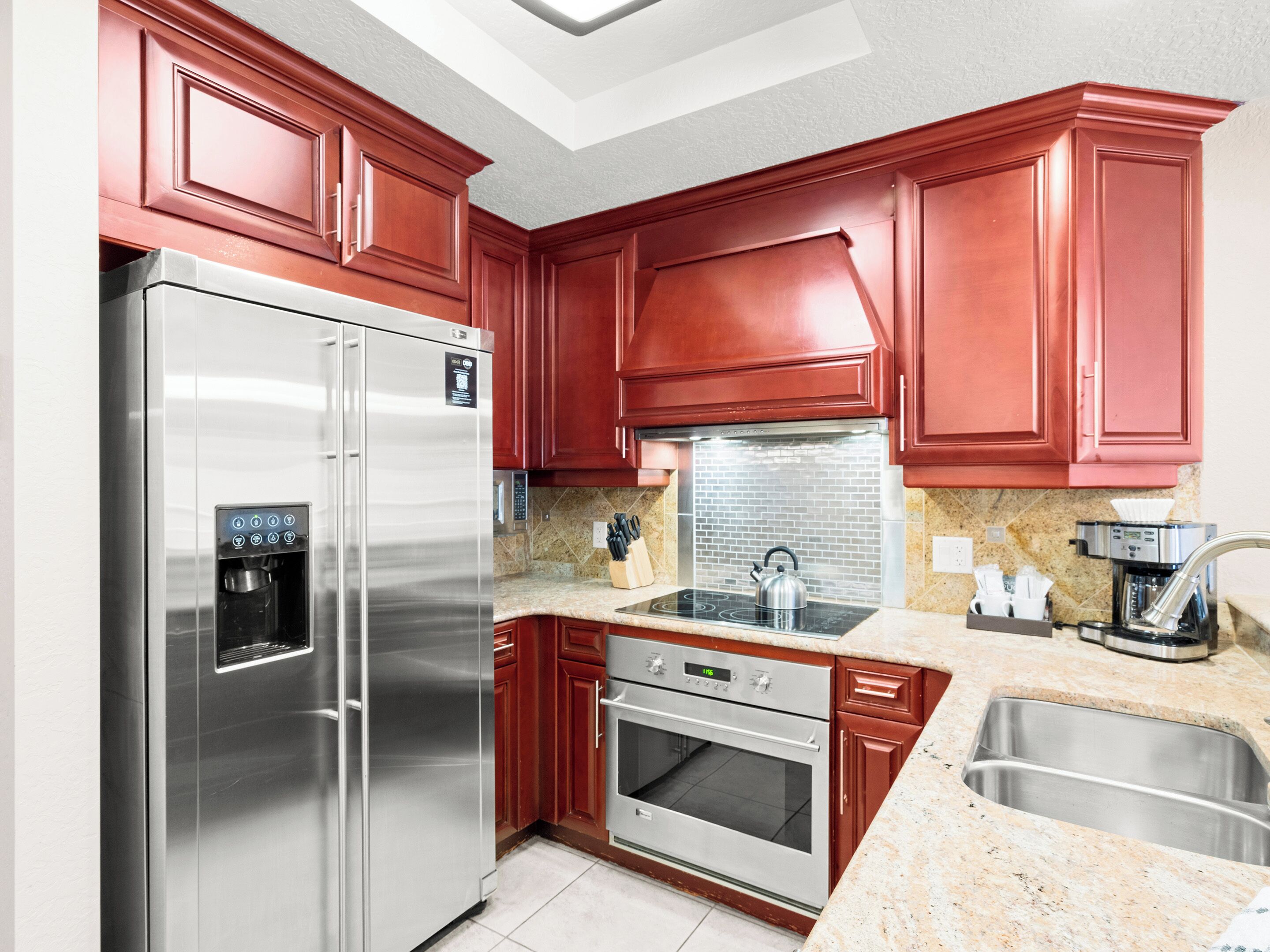 A modern kitchen with stainless steel appliances, red cabinetry, and granite countertops.