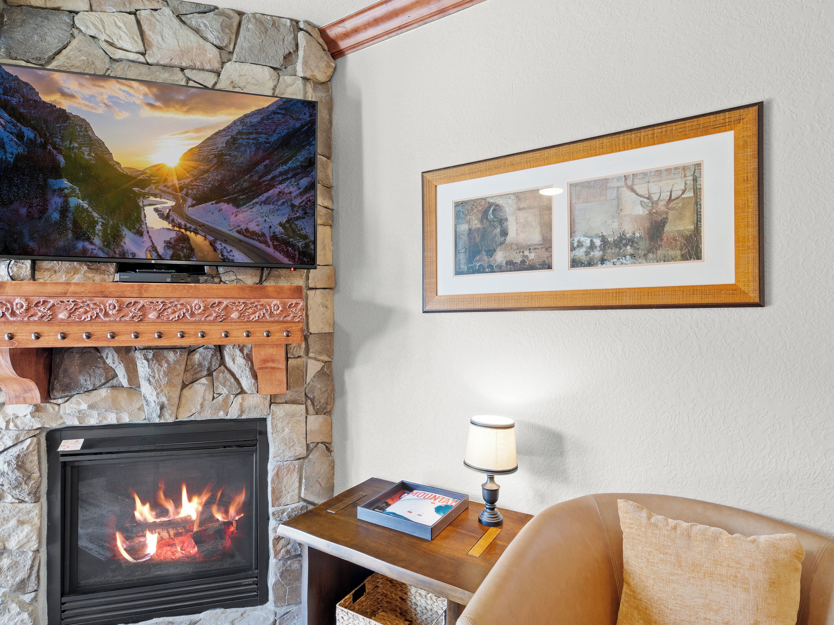 Ein Wohnzimmer mit Kamin aus Stein, einem flachbildfernseher darüber und einem gerahmten Bild an der Wand.