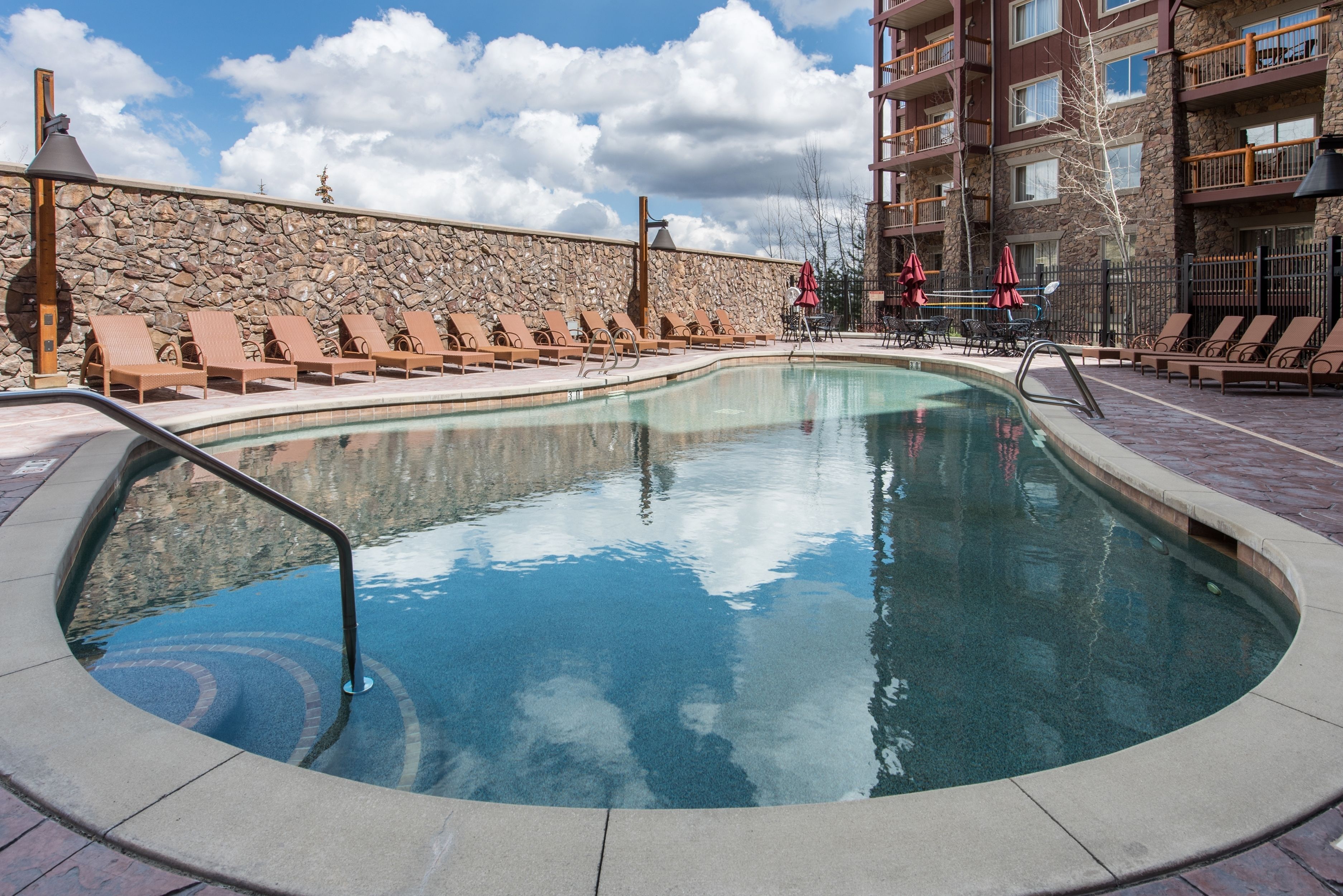 Una piscina con sillas de descanso y un muro de piedra.