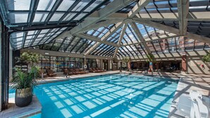 An indoor swimming pool with a glass ceiling, surrounded by lounge chairs and potted plants. - Canyons Village Condos by All Seasons Resort Lodging (Park City)
