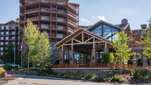 A multi-story hotel with a prominent entrance featuring a wooden pavilion and stone pillars. - Canyons Village Condos by All Seasons Resort Lodging (Park City)