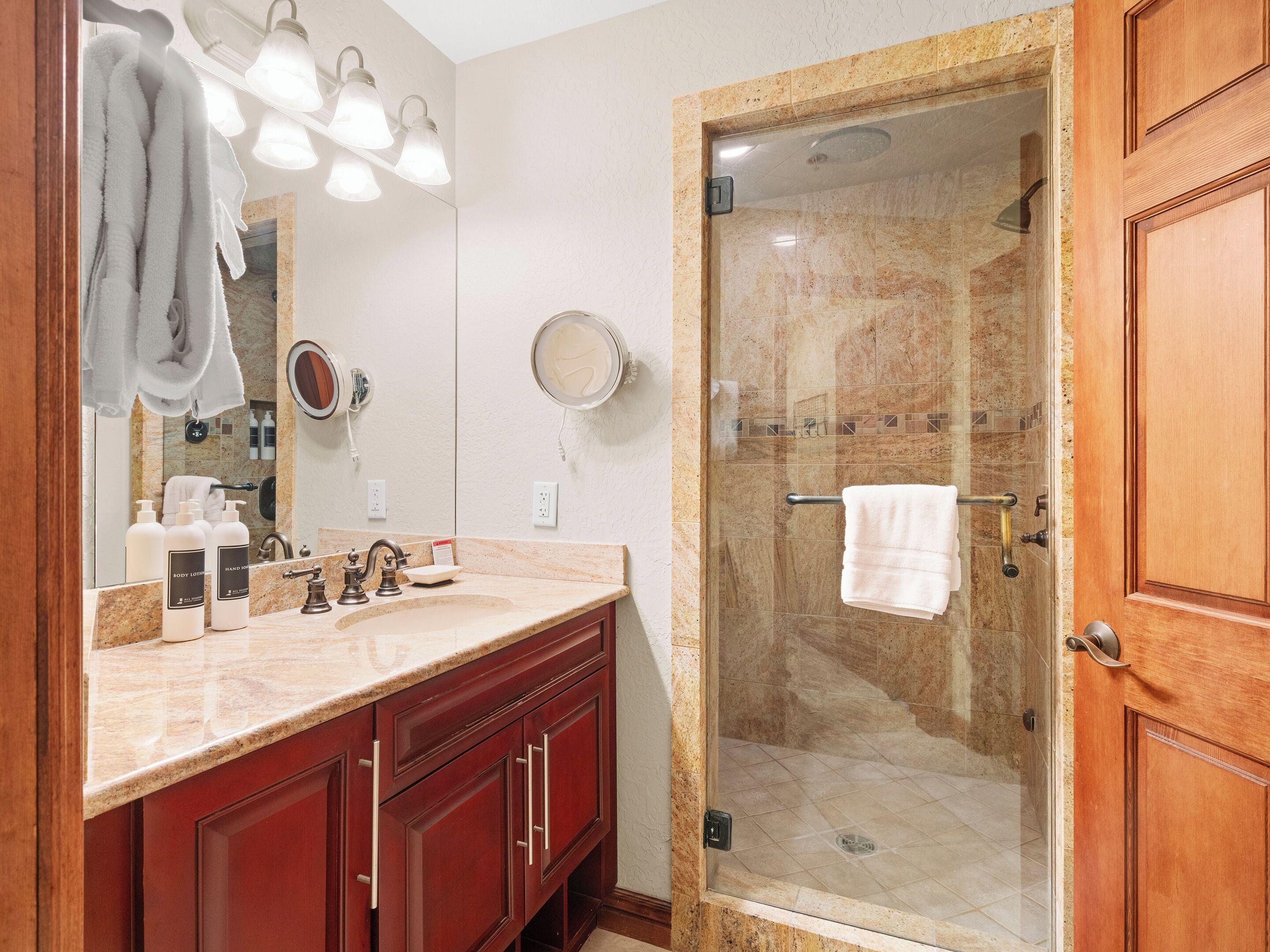 A bathroom with a marble sink, a glass-enclosed shower, and wooden cabinets.