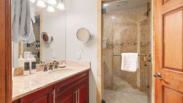 A bathroom with a marble sink, a glass-enclosed shower, and wooden cabinets.