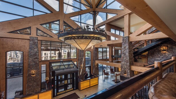 A spacious lobby with a high ceiling, stone pillars, and a central chandelier. - Canyons Village Condos by All Seasons Resort Lodging (Park City)