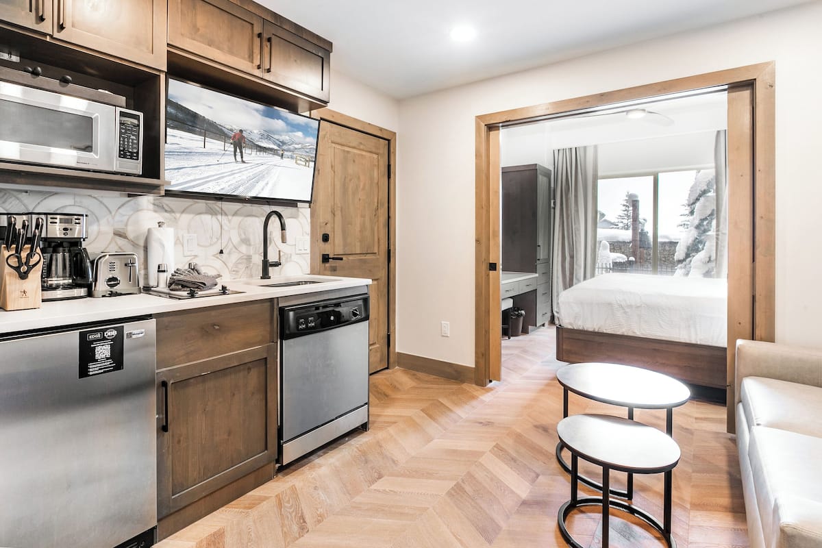 Una cocina compacta con electrodomésticos modernos, una zona de comedor con dos taburetes y vistas a un paisaje nevado a través de una puerta de cristal.