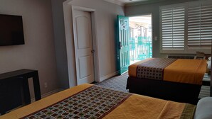 Una habitación de hotel con dos camas, un televisor, una puerta que da a un balcón y una ventana con persianas.