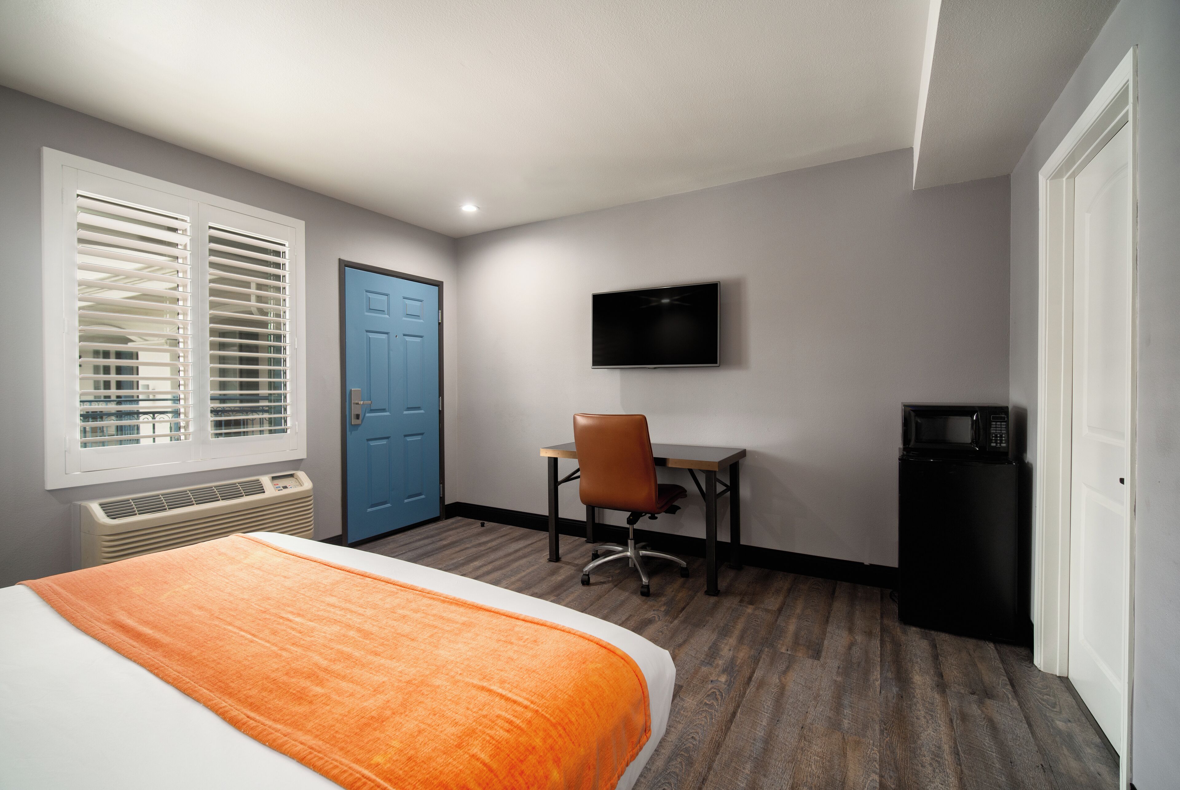 Una habitación de hotel con cama, escritorio con silla, televisor y microondas.
