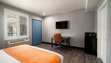 Una habitación de hotel con cama, escritorio con silla, televisor y microondas.