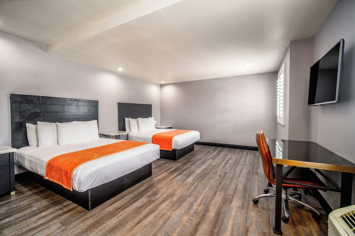 A hotel room with two beds, a desk, and a TV.