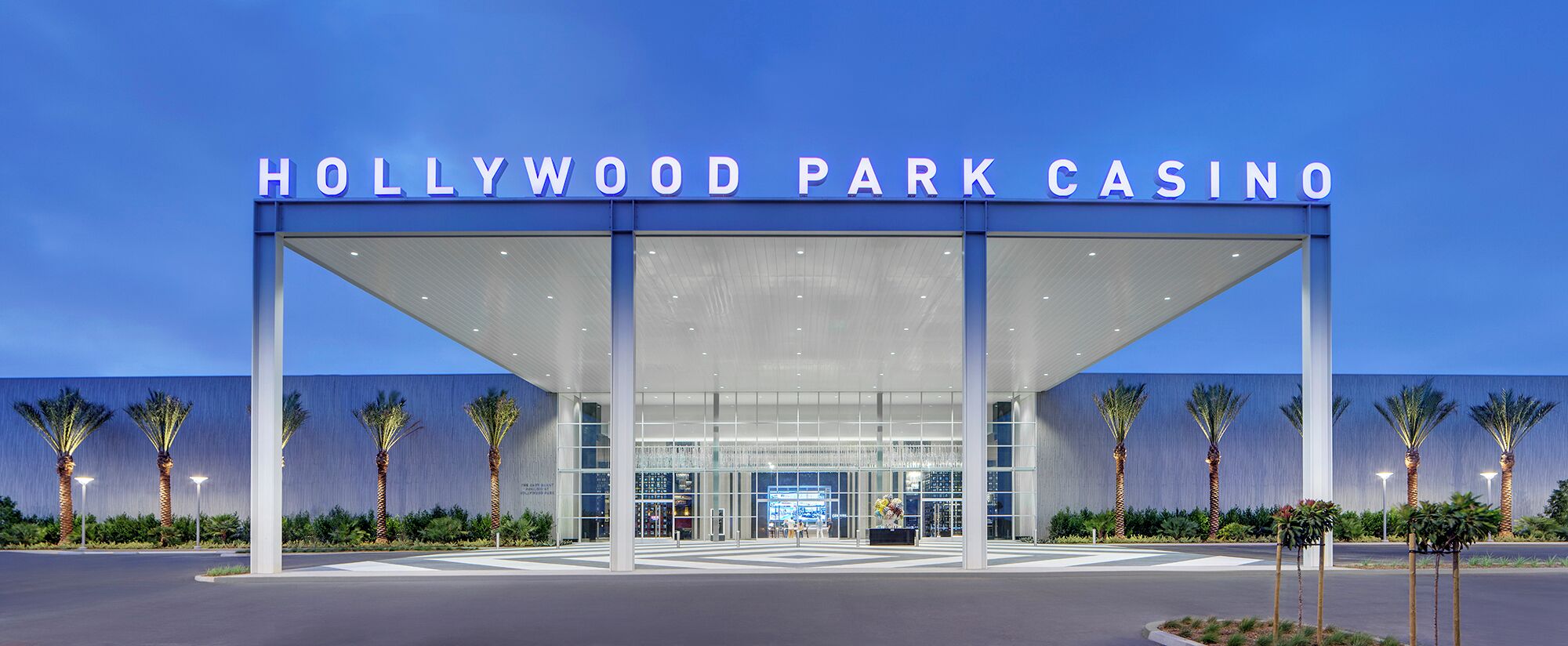 Entrada del Hollywood Park Casino con un diseño moderno, que incluye un amplio toldo y palmeras.