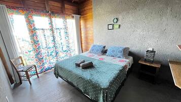 A bedroom with a bed, a chair, a small table, and a window with curtains.