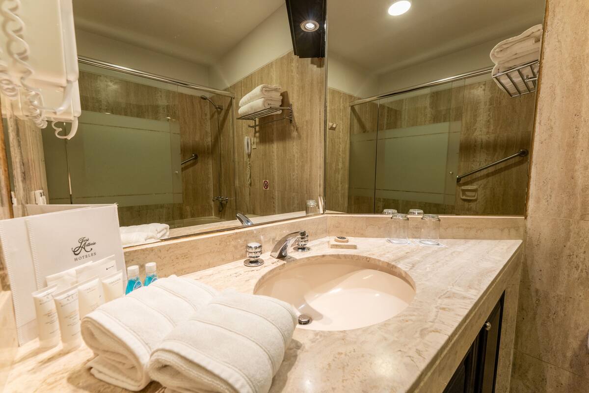 A hotel bathroom with a large mirror, a sink, and a shower area.