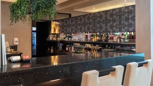 Un espace bar doté d’un comptoir en marbre noir, d’une variété de bouteilles d’alcool et d’une plante verte suspendue.