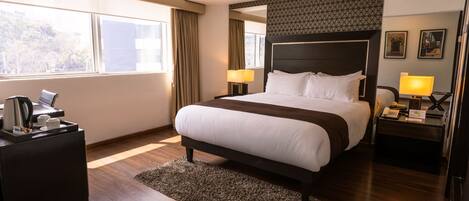 A hotel room with a large bed, bedside tables with lamps, a coffee maker, and a view of the outdoors.