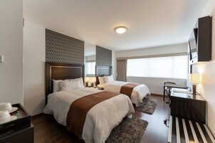 A hotel room with two beds, a desk, a chair, a TV, and a window with curtains.