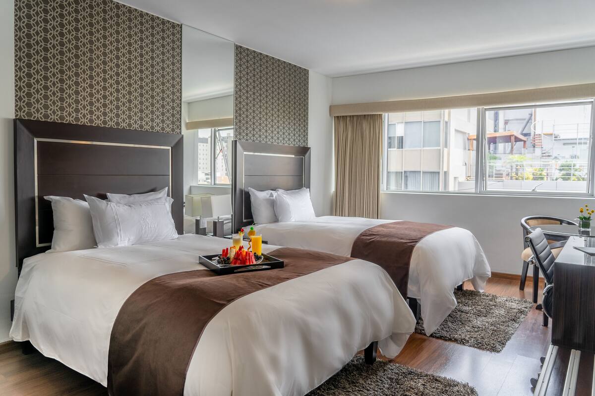 A hotel room with two beds, a dining area, and a view of the city.