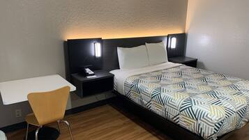 A hotel room with a bed, bedside table, chair, and a desk.