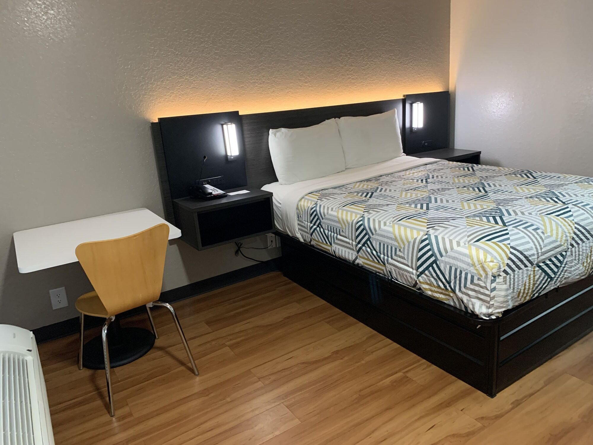A hotel room with a bed, bedside tables, a chair, and a desk.