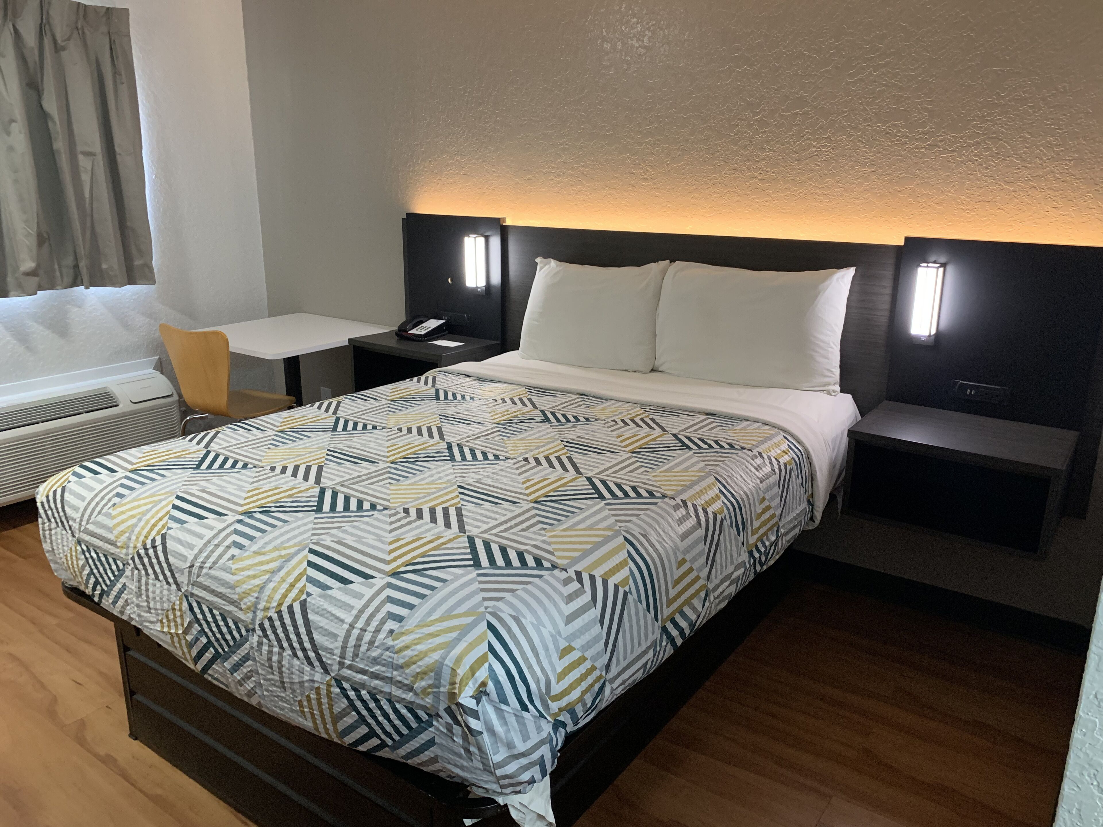 A hotel room with a bed, bedside tables, a desk, and a chair.