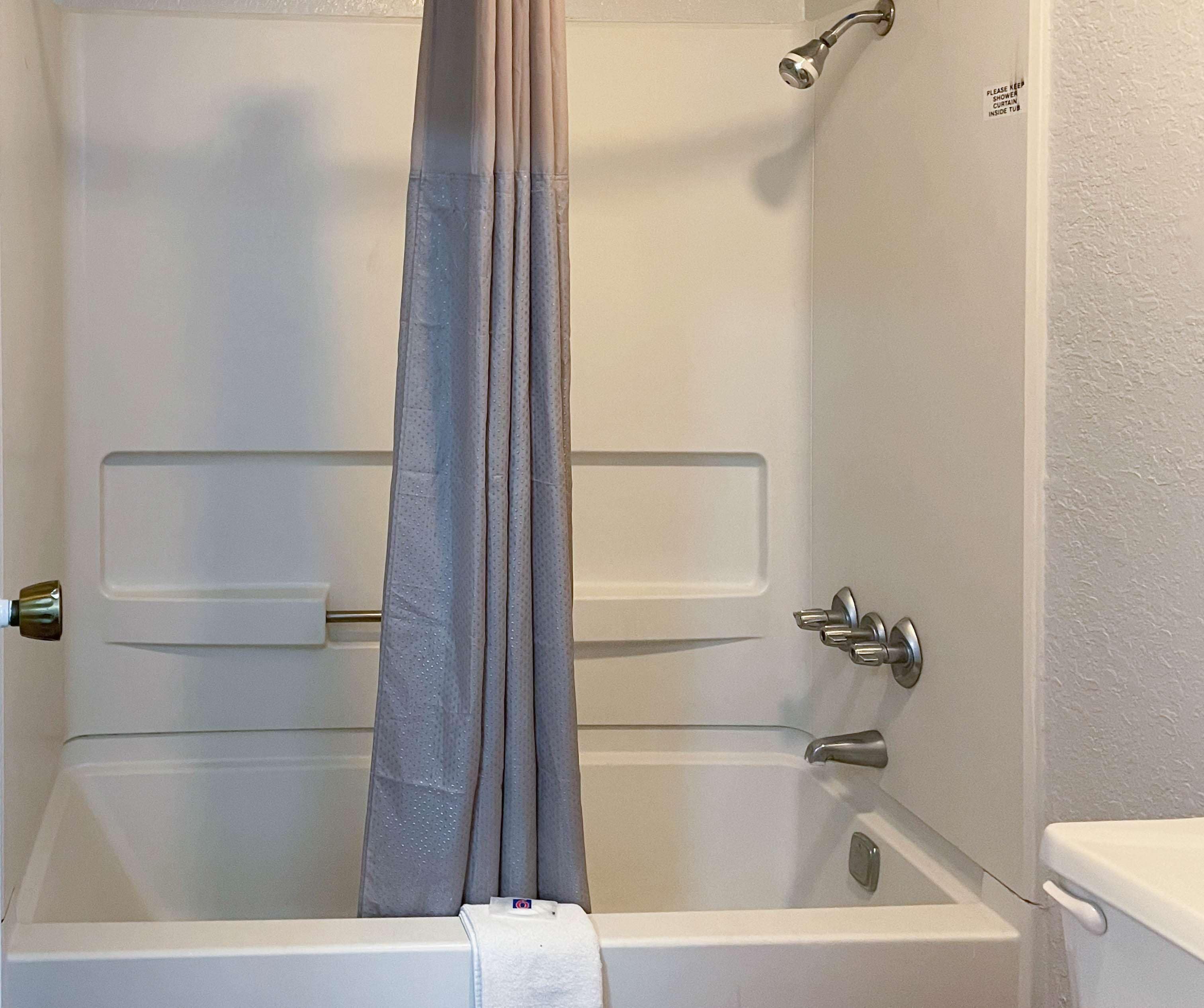 A white bathtub with a shower curtain, a towel, and a toilet visible.