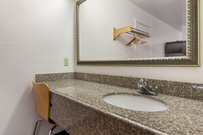 A bathroom with a granite countertop, a sink, a mirror with an ornate frame, and a towel rack. - Motel 6 Atlanta, TX (Atlanta)