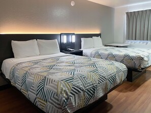 A hotel room with two beds, each with patterned bedding, a nightstand with a lamp, and a window with curtains. - Motel 6 Atlanta, TX (Atlanta)