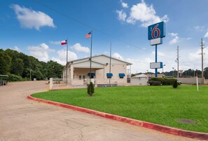 A motel with a large sign, a flag, and a grassy area. - Motel 6 Atlanta, TX (Atlanta)