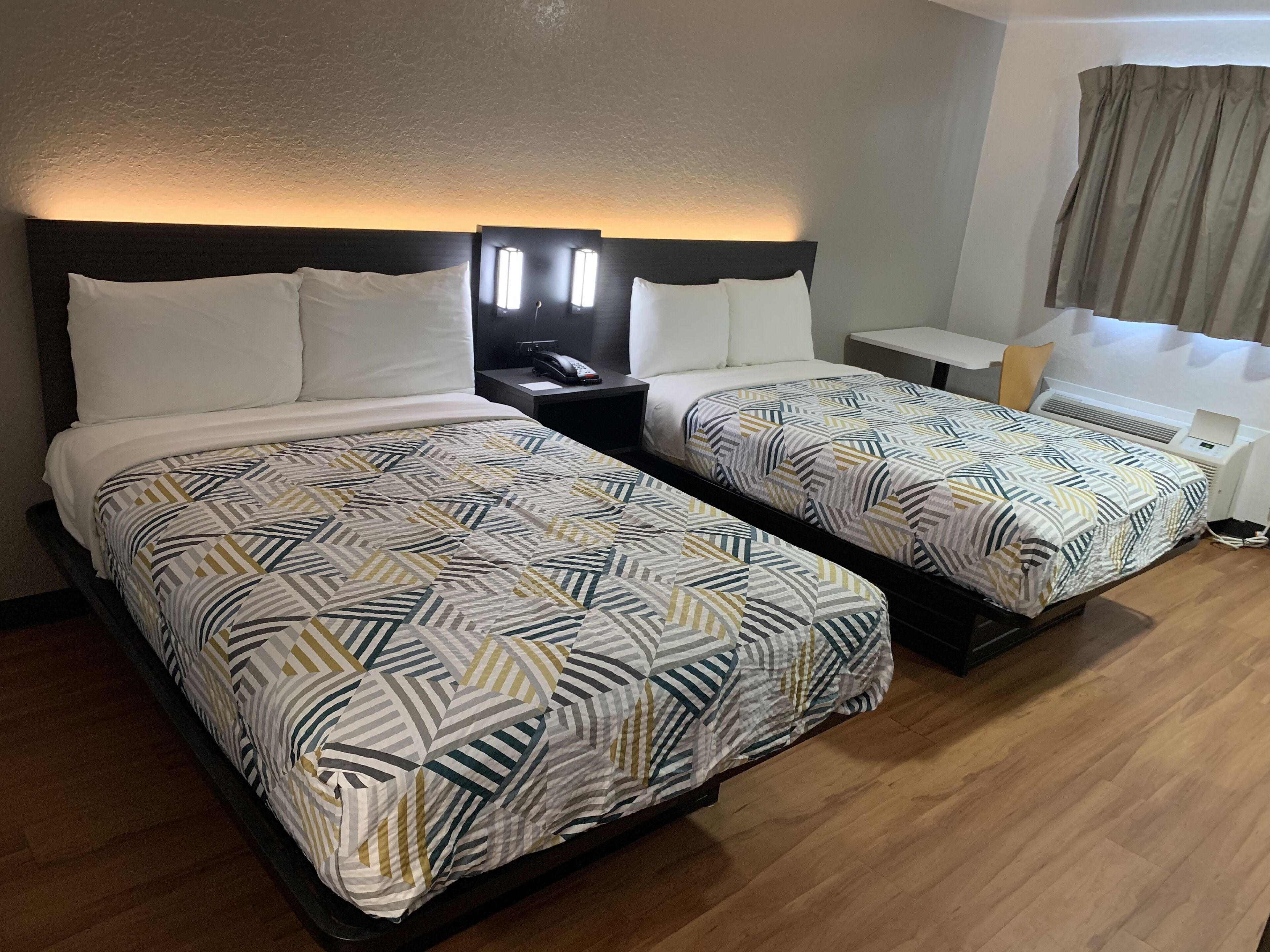 A hotel room with two beds, each with patterned bedding, a bedside table with a phone, and a nightstand with a lamp.