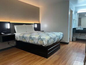 A modern hotel room with a bed, bedside table, and a bathroom visible through an open door. - Motel 6 Atlanta, TX (Atlanta)