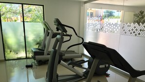 A gym with exercise equipment, including a treadmill and a stationary bike, in a room with large windows and a view of a fenced outdoor area.