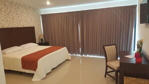 A hotel room with a large bed, a desk with a chair, and a window with curtains.