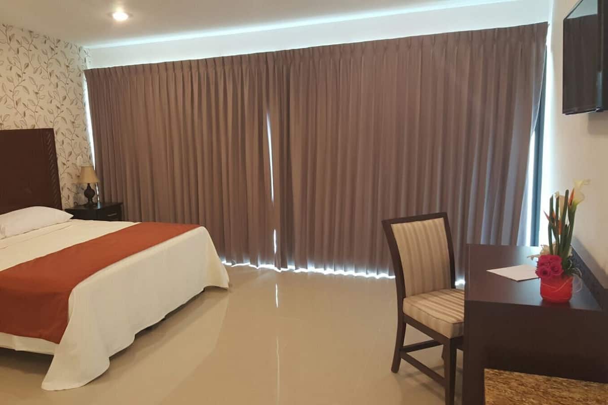 Ein Hotelzimmer mit einem großen Bett, einem Schreibtisch mit Stuhl und einem fensterbepflanzten Fenster.
