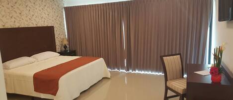 Una habitación de hotel con una cama grande, un escritorio con una silla y una ventana con cortinas.