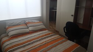 A bedroom with a bed, striped bedding, a chair, and a wardrobe. - Lima Flats 1 (Lima)