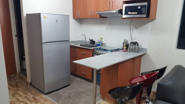 A compact kitchen with a refrigerator, microwave, stove, and a small dining area with a chair. - Lima Flats 1 (Lima)