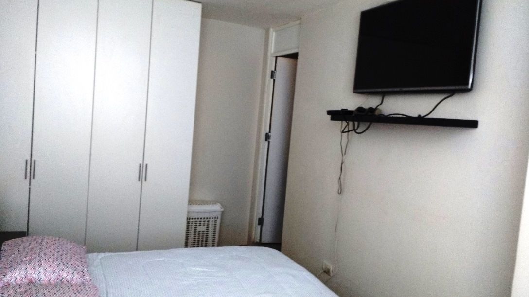 A bedroom with a bed, a wardrobe, a television mounted on the wall, and a laundry basket.