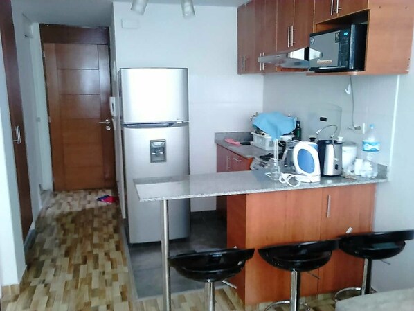 A compact kitchen with a refrigerator, microwave, and bar stools.