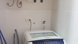 A compact laundry room with a white washing machine, a water heater, and a hose. - Lima Flats 4 (Lima)
