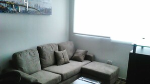 A living room with a grey sofa, a glass coffee table, and a painting of a bridge on the wall. - Lima Flats 4 (Lima)